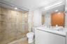 Walk-in shower with stone tile surround, glass sliding door, white vanity with integrated basin, polished metal hardware, and large vanity mirror