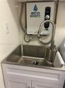 Stainless steel utility sink featuring a high-arc pull-down faucet, mounted above a white shaker-style vanity cabinet, accompanied by an electric tank