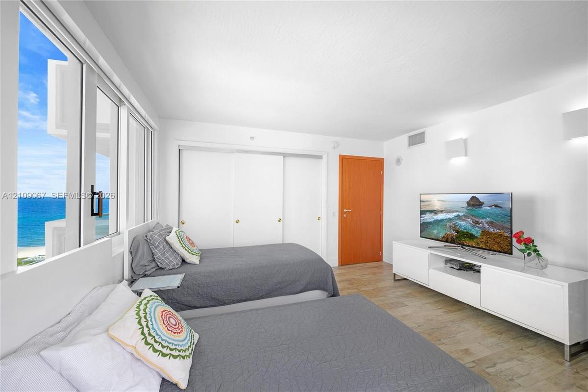 Floor-to-ceiling windows featuring ocean scenery, wood-finish flooring, sliding door closets, and wall-mounted light fixtures