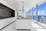 Contemporary kitchen featuring floor-to-ceiling windows, a center island with a dark stone countertop, minimalist flat-panel cabinetry, integrated rec