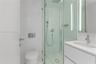 Bathroom featuring a glass-enclosed shower with a rainfall showerhead, wall-mounted dual-flush toilet, white vanity with an integrated sink, polished 