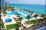 Extensive pool deck featuring multiple swimming pools, stone-paved terrace, built-in shaded cabanas, and manicured landscaping