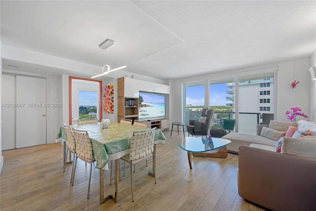 Open-concept living space featuring wood-finish flooring, floor-to-ceiling glass sliding doors, built-in media cabinetry with high-gloss finishes, and