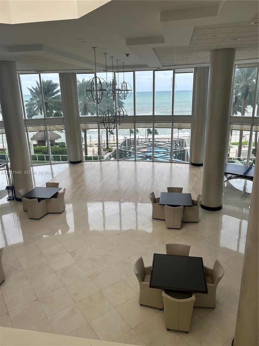 Double-height floor-to-ceiling windows, polished tile flooring, wood-finish flooring accents, structural cylindrical columns, and metal orb pendant li