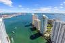 Aerial perspective of waterfront urban skyline featuring high-rise buildings, deep-water channel, maritime traffic, and proximity to expansive harbor 