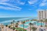 Oceanfront terrace featuring multiple swimming pools, stone-paved decking, built-in pergolas, and established palm trees