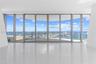 Floor-to-ceiling glass walls, expansive curved balcony with a glass railing, polished tile flooring, and structural white pillars