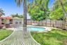 In-ground swimming pool with stone-style paver decking, enclosed by a wood privacy fence and featuring mature palm trees