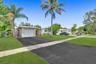 Single-story residence featuring a paved driveway, attached garage, stone facade accents, and mature palm trees