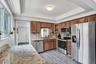 Kitchen featuring wood cabinetry, stone countertops, stainless steel appliances, and wood-finish flooring under a tray ceiling
