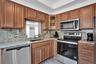 Kitchen featuring wood cabinetry, stone countertops, stainless steel appliances, a glass-panel cabinet door, and a pass-through window