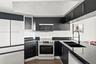 Modern kitchen featuring matte black cabinetry with gold-toned hardware, dark stone countertops, an integrated microwave, a high-arc faucet, and wood-