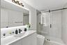 Bathroom featuring a white vanity with an integrated sink, matte black faucet, full-width mirror with integrated lighting, and a glass-enclosed shower