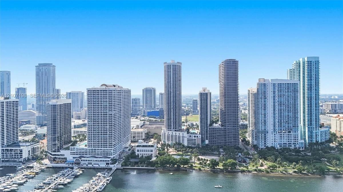 High-rise urban landscape featuring a dense skyline of multi-story glass-facade buildings, a waterfront marina with boat slips, and interspersed areas
