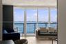 Floor-to-ceiling windows featuring panoramic water and city skyline outlooks, wood-finish flooring, and a private balcony with a metal railing
