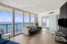 Floor-to-ceiling windows, wood-finish flooring, balcony with metal railing, and a dark vertical-slat accent wall