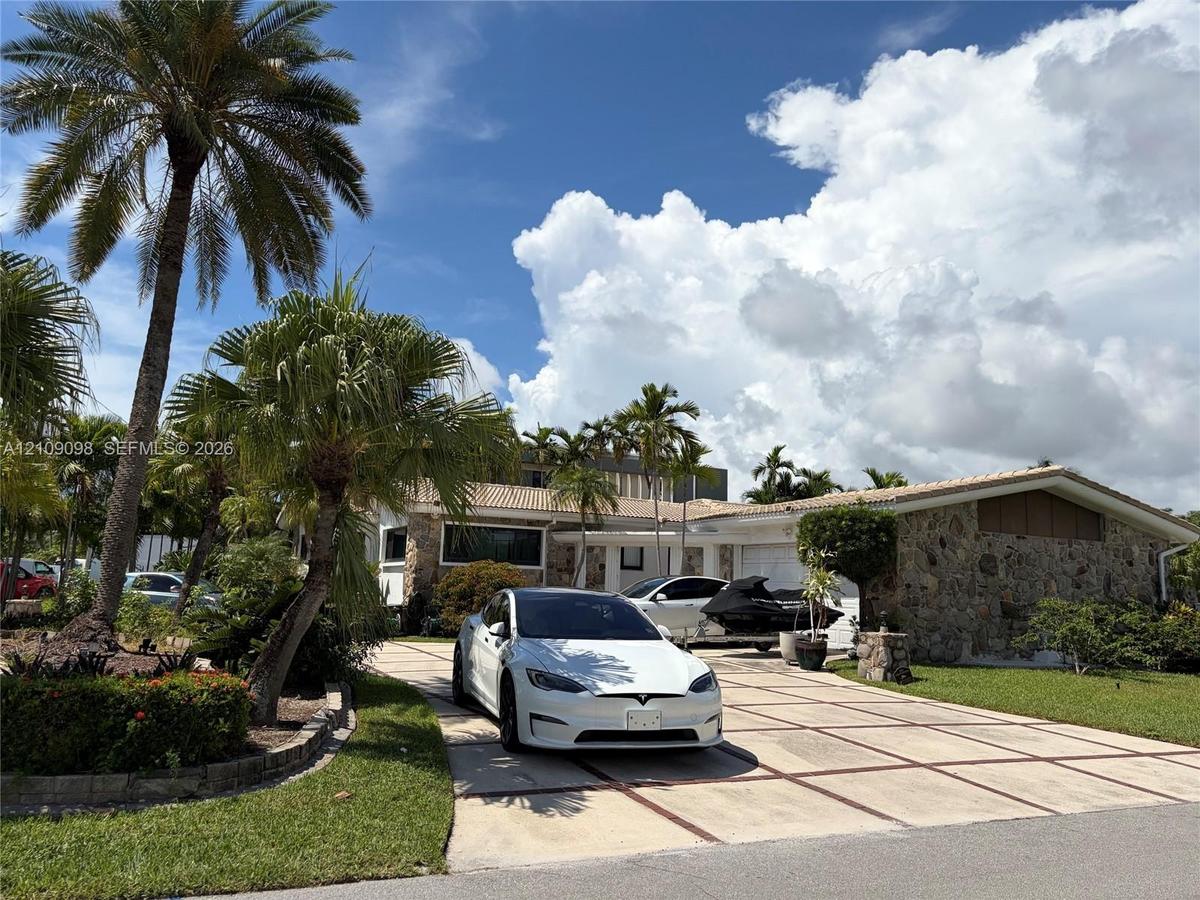Single-story exterior featuring natural stone facade, grid-patterned concrete driveway, and established palm landscaping