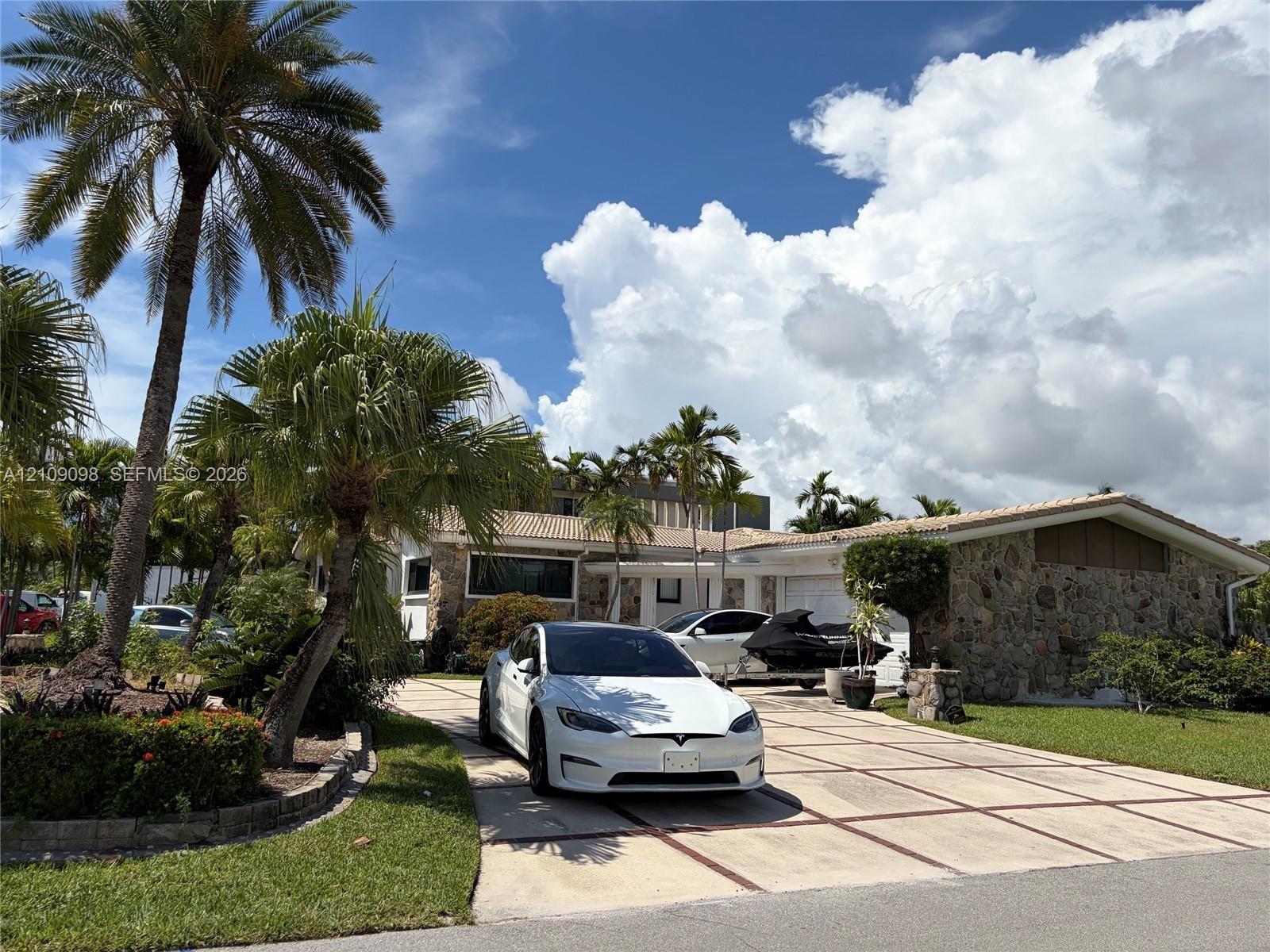 Single-story exterior featuring natural stone facade, grid-patterned concrete driveway, and established palm landscaping