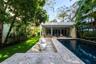 Outdoor living area featuring a custom swimming pool with stone decking, integrated landscape design, and a flat-roofed structure with floor-to-ceilin