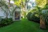 Private exterior space featuring synthetic turf, structured louvered window detailing, white stucco wall surfaces, mature tropical landscaping, and la