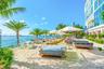Waterfront sandy beach area featuring glass perimeter railing, mature palm trees, and structural concrete building exterior
