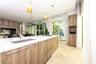 Kitchen featuring an island with a stone-finish countertop, undermount sink, wood-finish cabinetry, recessed lighting, and floor-to-ceiling glass slid