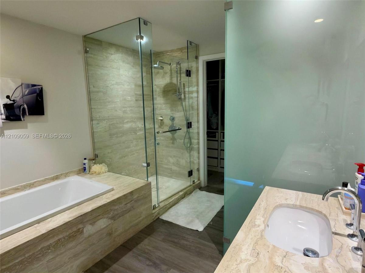 Bathroom featuring a soaking tub with stone-finish surround, glass-enclosed shower with adjustable rainfall showerhead, stone-finish vanity countertop