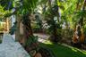 Outdoor area featuring stone-clad structural pillars, natural stone paving, mature tropical landscaping, and a built-in privacy fence