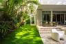 Natural stone paved patio featuring a built-in step, multi-panel sliding glass doors, horizontal exterior louvers, and a bordering artificial turf law