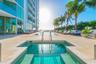 Pool deck featuring an in-ground spa, stone-finish paving, full-height glass building exterior, and palm tree landscaping