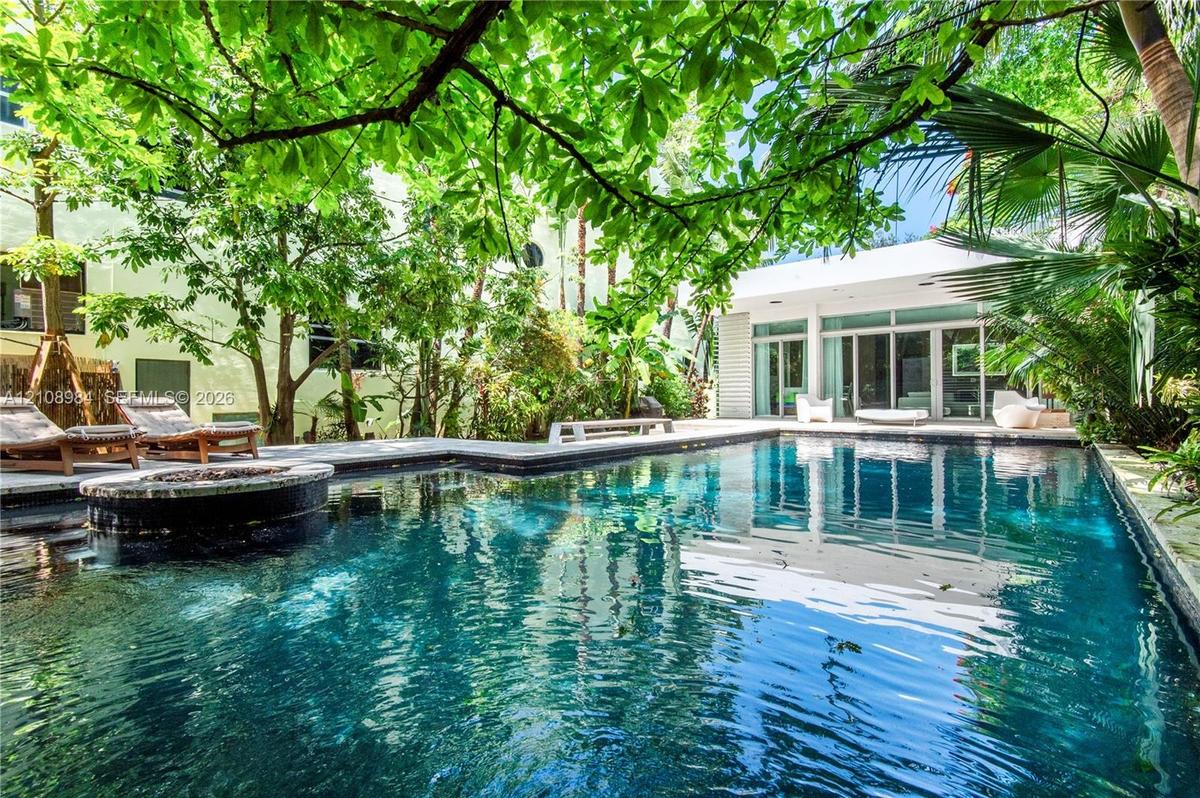 In-ground swimming pool featuring stone coping and a circular integrated spa, surrounded by mature trees, lush tropical landscaping, and expansive sto