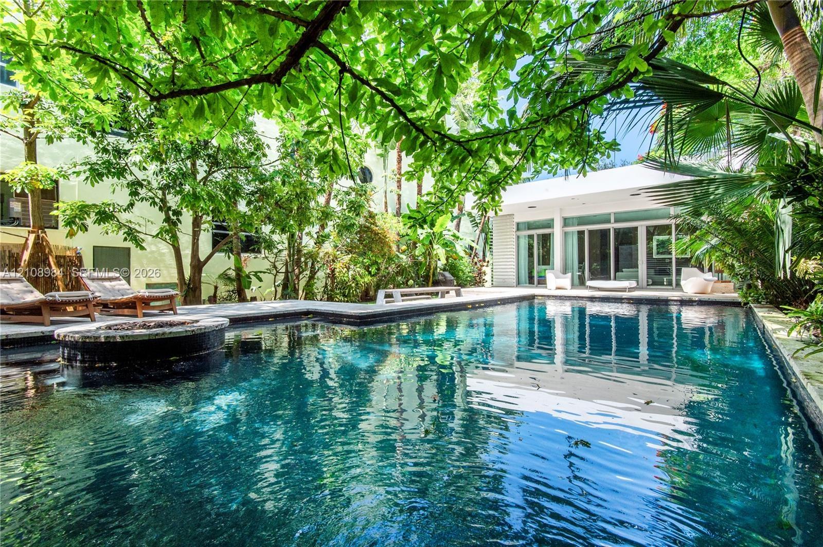 In-ground swimming pool featuring stone coping and a circular integrated spa, surrounded by mature trees, lush tropical landscaping, and expansive sto