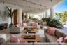 Covered outdoor lounge area featuring recessed track lighting, structural columns, a built-in wet bar, stone flooring, and water-facing orientation