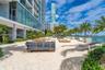 Outdoor terrace featuring a sandy surface, glass panel railings, mature palm trees, and structural concrete columns