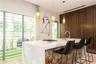 Kitchen island with stone countertop, waterfall edge, and built-in cooktop, paired with full-height wood-finish cabinetry and three pendant lights