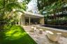 Outdoor space featuring a swimming pool, natural stone patio, covered terrace, and manicured lawn surrounded by mature palms and foliage