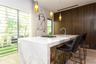 Waterfall-edge stone island with integrated cooktop and undermount sink, floor-to-ceiling wood-finish cabinetry, triple glass pendant lighting, and fu