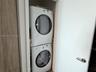 Stacked front-loading laundry unit enclosed in a dedicated closet featuring wood-finish cabinetry
