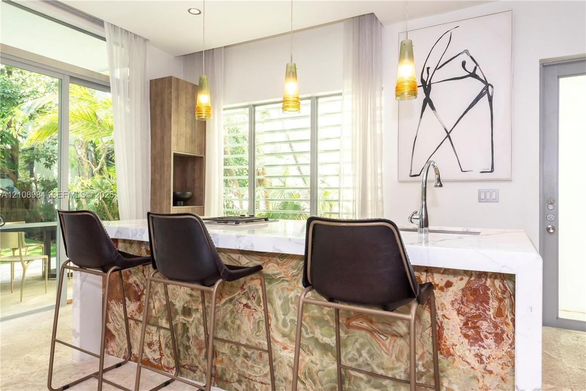 Kitchen island with a stone-finish facade, white countertop with waterfall edge, integrated cooktop, stainless steel gooseneck faucet, and three penda