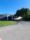 Single-story residence featuring a metal roof, attached garage, paved driveway, and mature landscaping