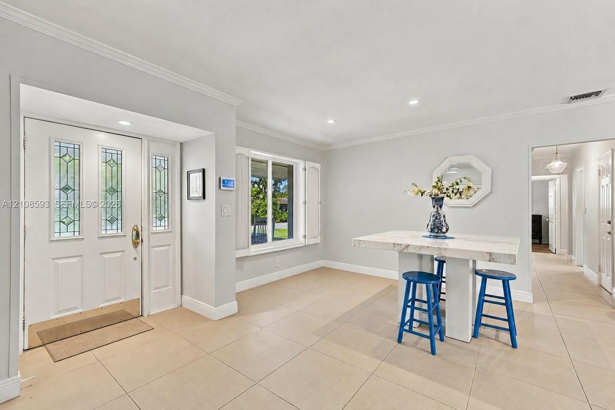 Entryway featuring a white door with decorative glass panels, neutral tile flooring, recessed lighting, crown molding, and window shutters