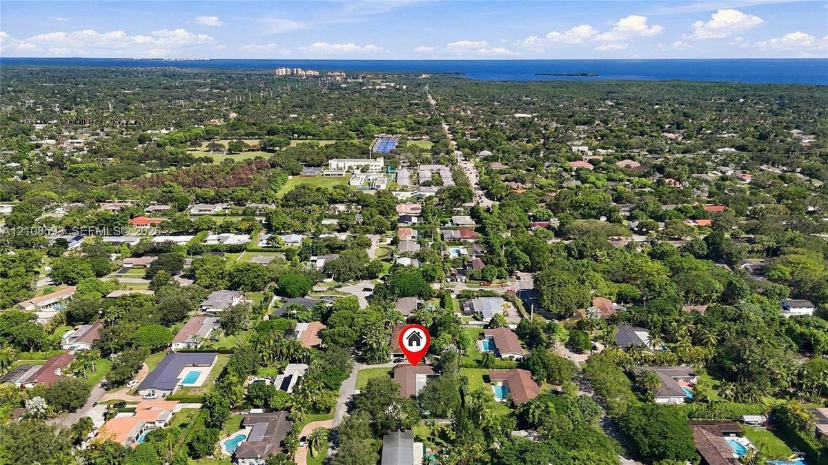 Aerial perspective of a residential property situated in a coastal region with extensive tree canopy and proximity to the waterfront