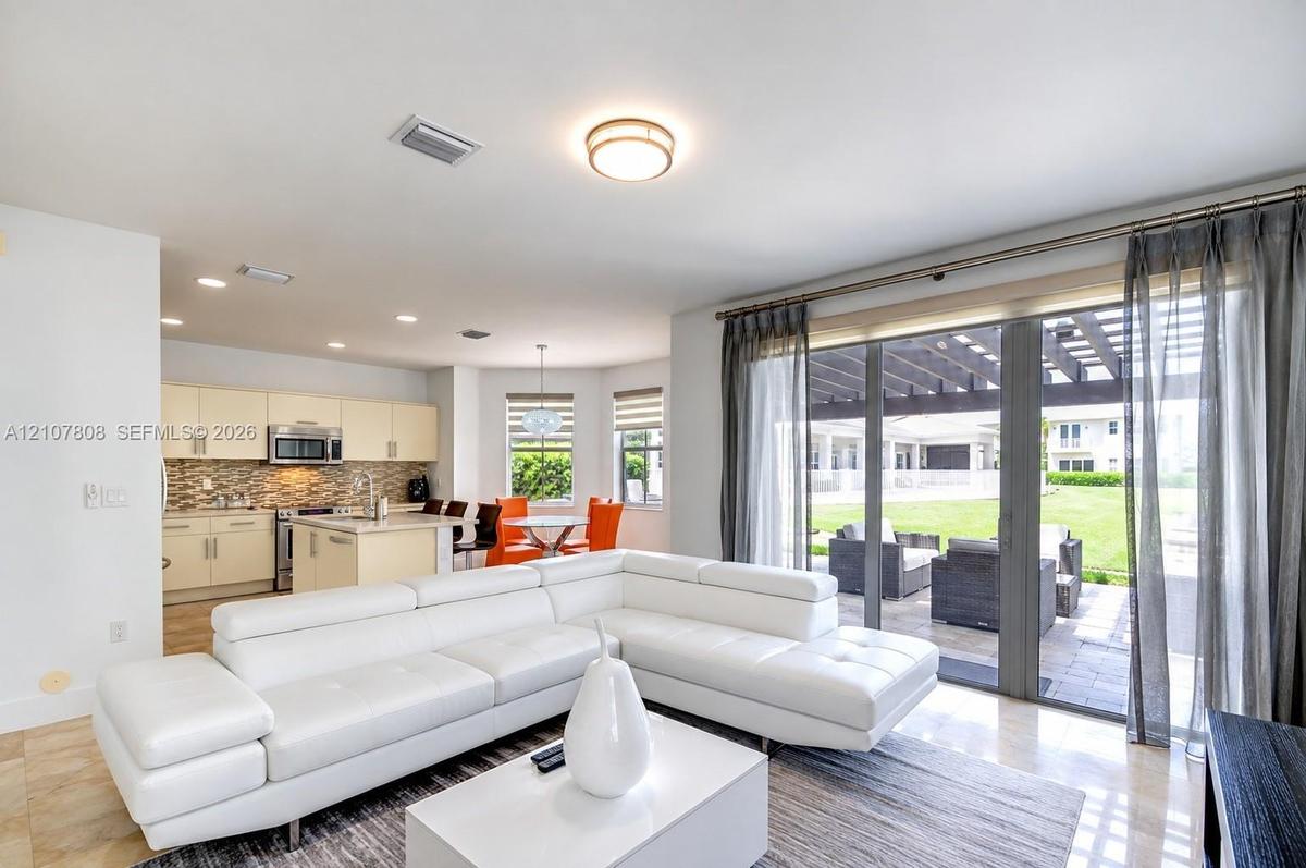 Open-concept interior featuring large-format stone flooring, recessed lighting, kitchen with light-toned cabinetry, and floor-to-ceiling sliding glass