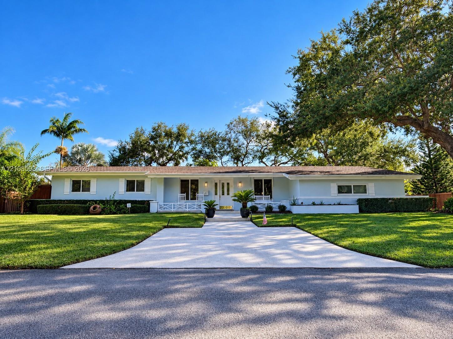 Single-story residence featuring light-toned exterior cladding, a paved walkway, covered front porch with decorative railing, and manicured landscapin