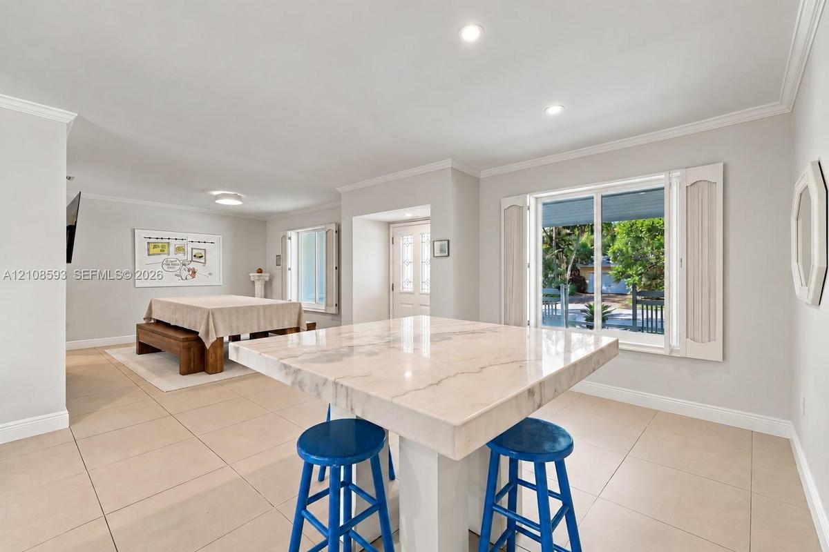 Open-concept interior featuring large-format tile flooring, recessed ceiling lighting, a central stone-top island, and dual windows equipped with plan