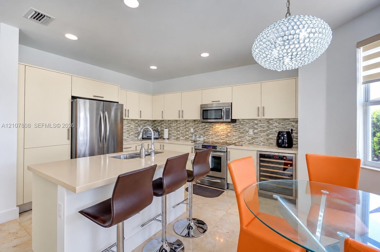 Kitchen featuring flat-panel cabinetry, quartz countertops, a mosaic tile backsplash, stainless steel appliances including a built-in wine cooler, and