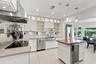 Kitchen featuring white cabinetry with glass-front uppers, stainless steel farmhouse sink, professional-grade range hood, butcher-block topped island 