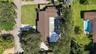 Aerial perspective featuring a multi-pitched shingle roof, paved driveway, expansive lawn, and mature trees
