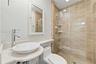 Bathroom featuring a white oval vessel sink, chrome high-arc faucet, solid surface countertop, walk-in shower with floor-to-ceiling tile, and frameles