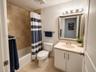 Bathroom featuring tile-surround bathtub, solid-surface vanity countertop, white cabinet storage, ceramic tile flooring, and wall-mounted vanity light